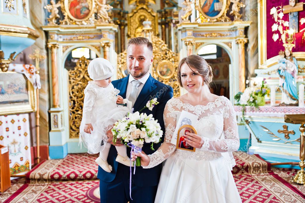 Happy wedding couple in the church with their little baby daught