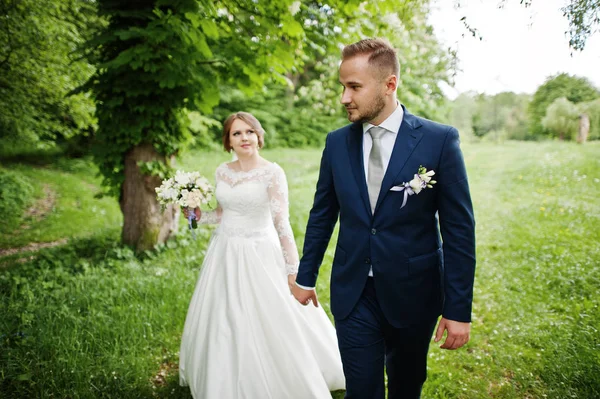 Casal de casamento incrível andando e posando em algum lugar no verde — Fotografia de Stock