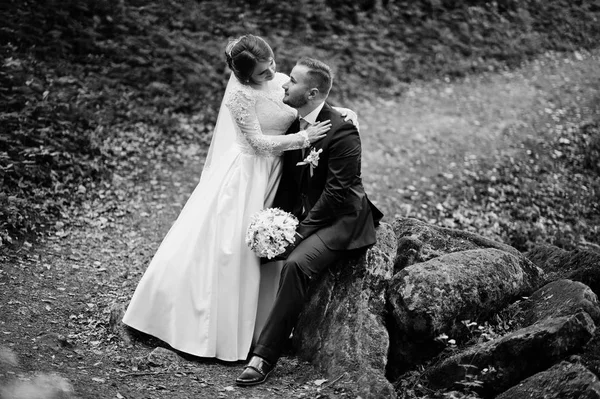 Magnífica noiva sentada em um colo do marido na floresta — Fotografia de Stock