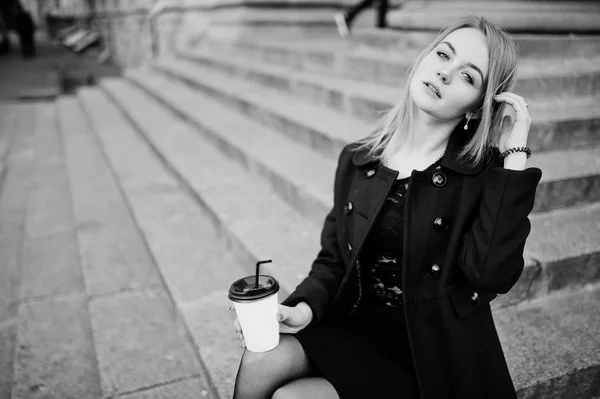 Elegant blond flicka bära på svart poserar på gatorna i staden, sitta — Stockfoto