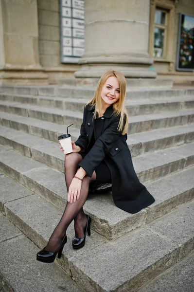 Elegante chica rubia llevar en negro posando en las calles de la ciudad, sentarse — Foto de Stock