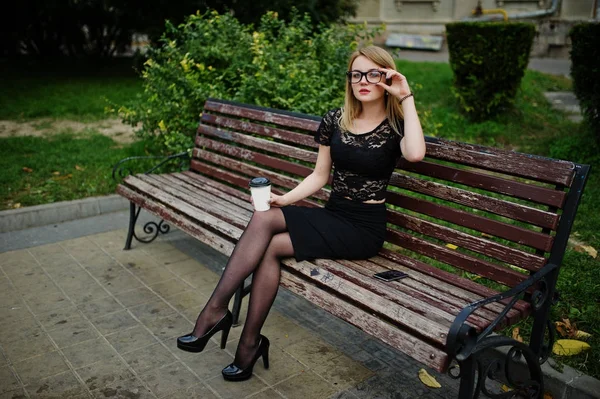 Elegante chica rubia llevar en negro posando en las calles de la ciudad, sentarse —  Fotos de Stock
