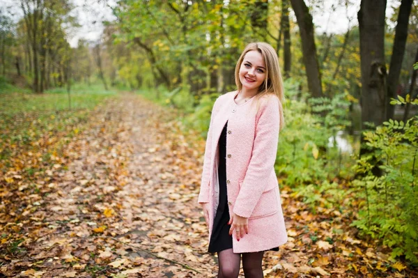 Giovane ragazza bionda a cappotto rosa posato sul parco autunnale . — Foto Stock