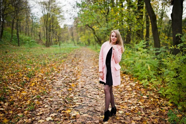 Молодая блондинка в розовом пальто позировала в осеннем парке . — стоковое фото