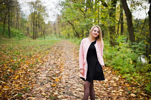 Jong blond meisje op roze jas gesteld op herfst park. — Stockfoto