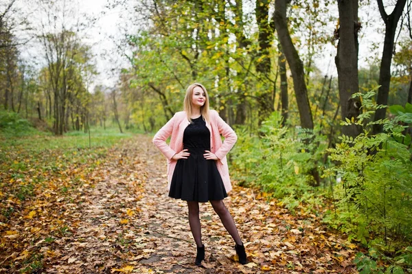 Ung blond tjej på rosa kappa som poseras på hösten park. — Stockfoto