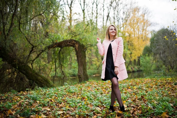 Ung blond tjej på rosa kappa som poseras på hösten park. — Stockfoto