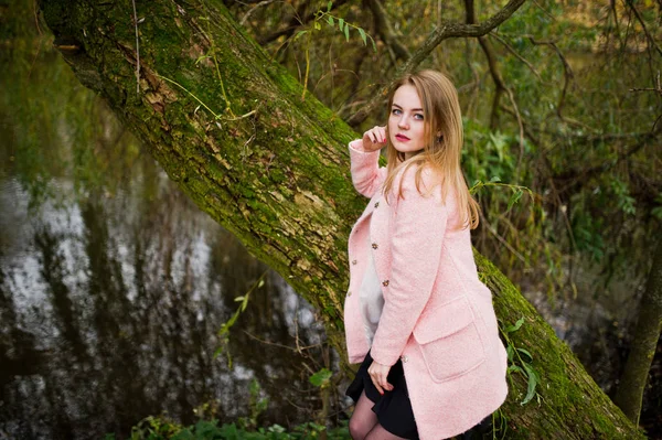 Jong blond meisje op roze jas gesteld op herfst park. — Stockfoto