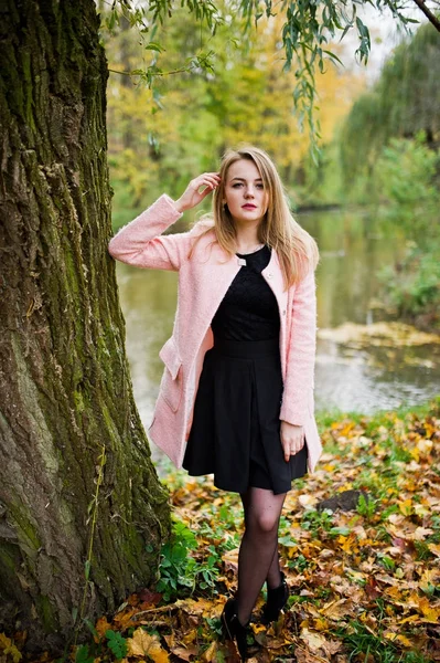 Νεαρή ξανθιά κοπέλα στο ροζ παλτό που θέτεται στο πάρκο φθινόπωρο. — Φωτογραφία Αρχείου