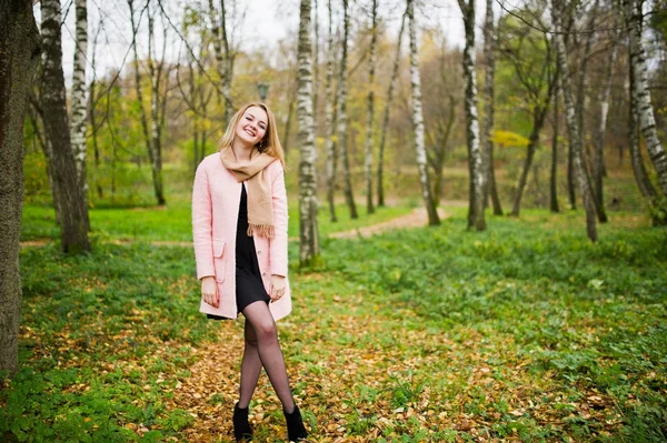 Mladá blondýnka v růžový kabát představuje na podzim park. — Stock fotografie