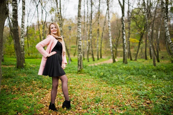 Ung blond tjej på rosa kappa som poseras på hösten park. — Stockfoto