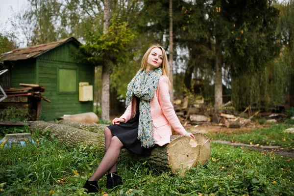 Jong blond meisje op roze jas gesteld op herfst park, zittend op — Stockfoto