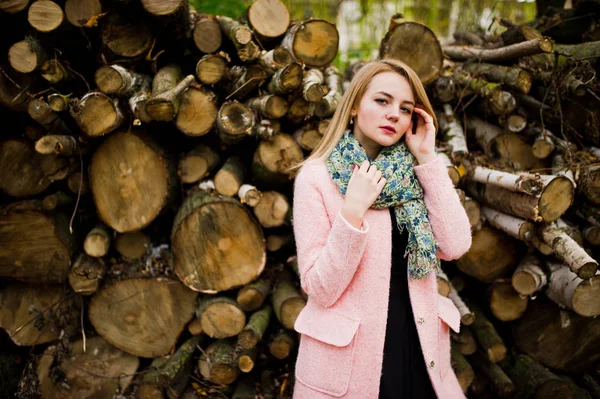 Joven chica rubia en el abrigo rosa posado contra tocones de madera espalda —  Fotos de Stock