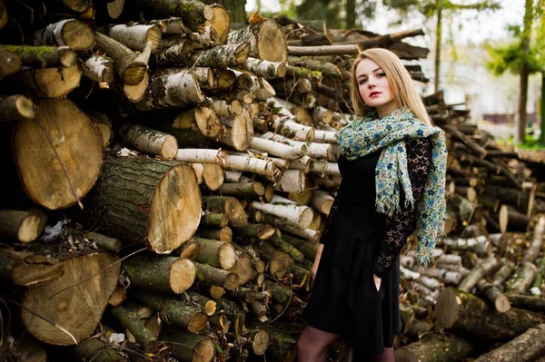 Joven chica rubia en negro con bufanda posado contra muñón de madera —  Fotos de Stock