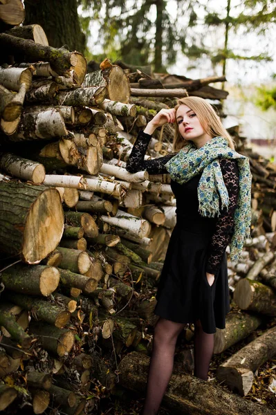 Young blonde girl at black with scarf posed against wooden stump — Stock Photo, Image