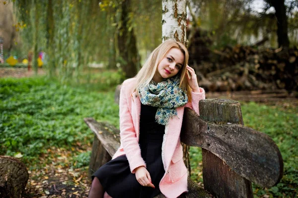 Jong blond meisje op roze jas zitten op bankje gesteld tegen wo — Stockfoto