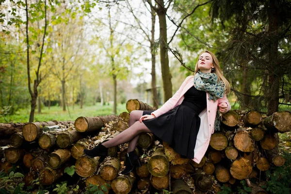 Молодая блондинка в розовом пальто позирует против деревянных пней назад — стоковое фото