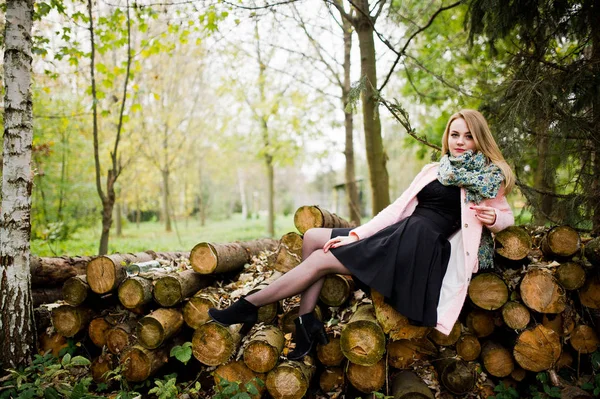 Молодая блондинка в розовом пальто позирует против деревянных пней назад — стоковое фото