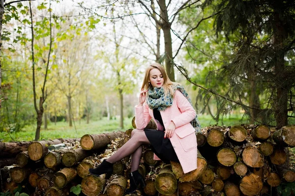 Jong blond meisje op roze jas gesteld tegen houten stompen backg — Stockfoto