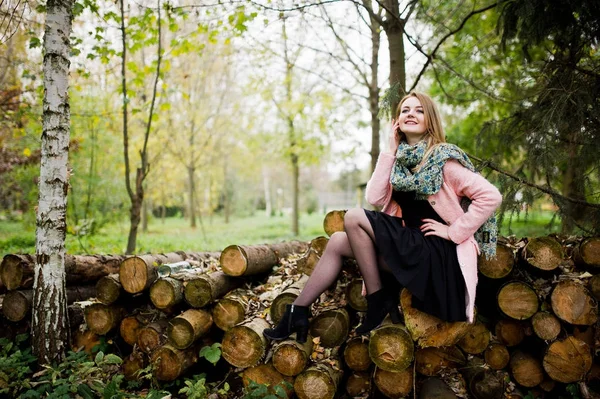 Jong blond meisje op roze jas gesteld tegen houten stompen backg — Stockfoto