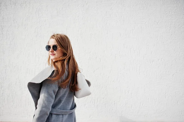 Chica en abrigo gris con gafas de sol y bolso de estancia contra el blanco —  Fotos de Stock