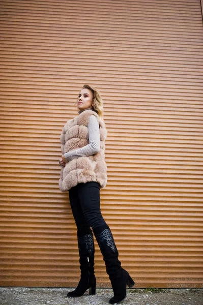 Blonde girl at fur coat against wall with shutters. — Stock Photo, Image