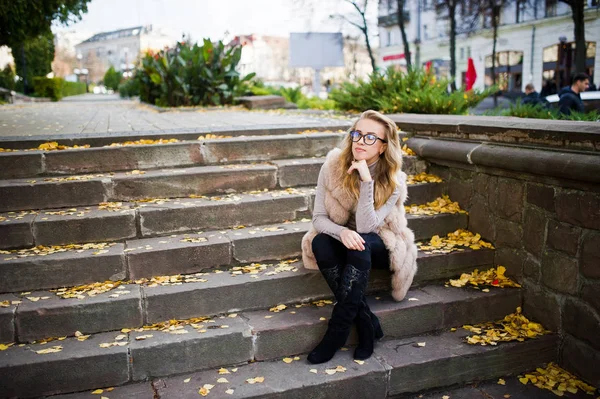 Blond flicka på päls och glasögon som sitter på trappan med yello — Stockfoto