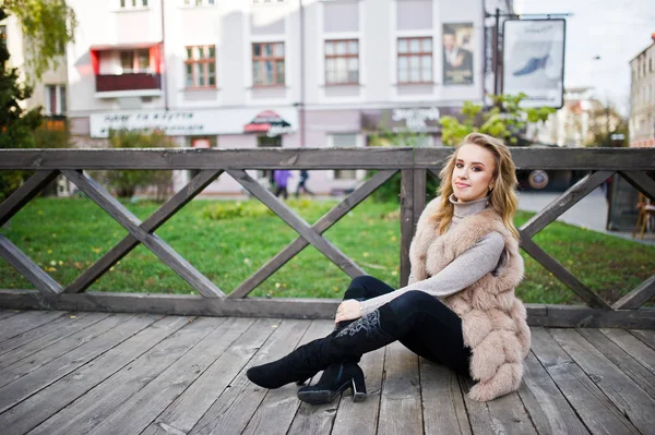 Blondes Mädchen im Pelzmantel sitzt auf Holzboden im Freien. — Stockfoto