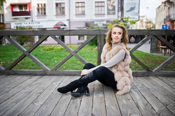 Chica rubia en abrigo de piel sentado en el suelo de madera al aire libre . — Foto de Stock