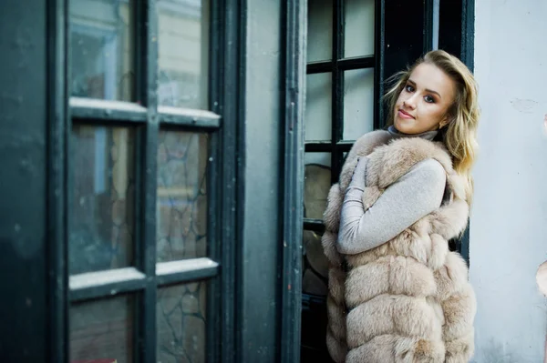 Chica rubia en abrigo de piel posado contra la vieja puerta de madera . — Foto de Stock
