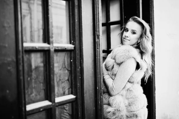 Блондинка в меховом пальто позировала перед старой деревянной дверью . — стоковое фото