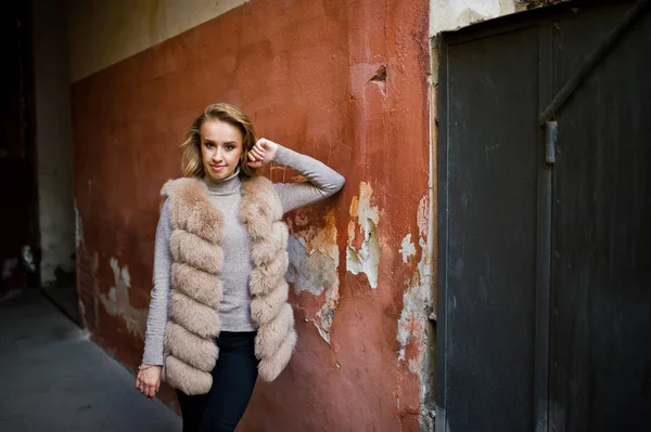 Chica rubia en abrigo de piel posado contra la vieja pared naranja . — Foto de Stock
