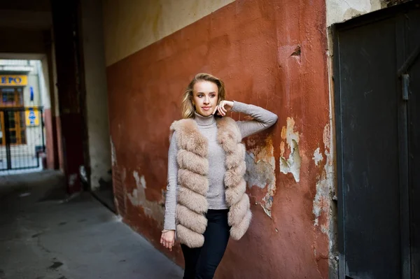 Blonde girl at fur coat posed against old orange wall. — Stock Photo, Image
