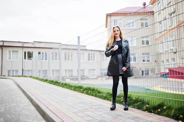 Blondes modisches Mädchen im langen schwarzen Ledermantel gegen Eisen — Stockfoto