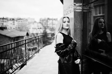 Uzun siyah deri montlu sarışın moda kız karşı poz verdi