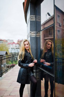 Uzun siyah deri montlu sarışın moda kız karşı poz verdi