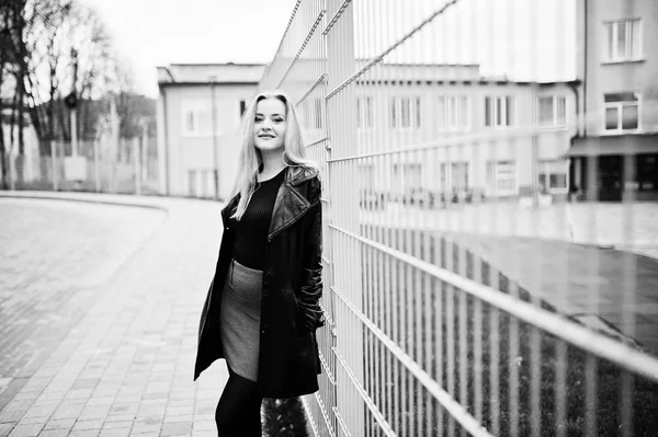 Blonde fashionable girl in long black leather coat against iron — Stock Photo, Image