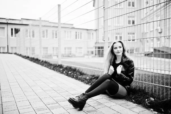 Blonde fashionable girl in long black leather coat against iron — Stock Photo, Image