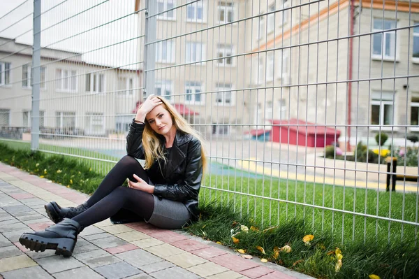 Blonde fashionable girl in long black leather coat against iron — Stock Photo, Image