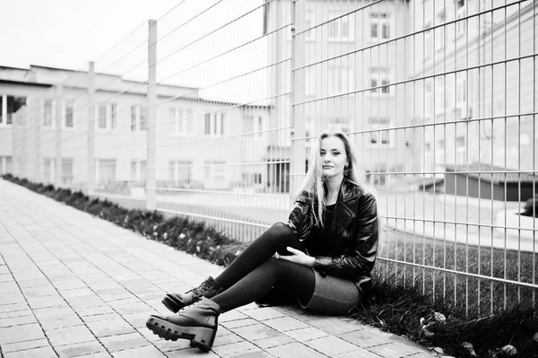 Blonde fashionable girl in long black leather coat against iron — Stock Photo, Image