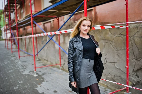 Blondes modisches Mädchen im langen schwarzen Ledermantel posierte am Strand — Stockfoto