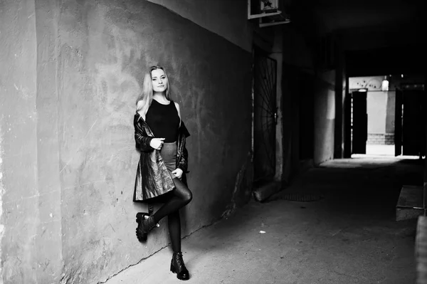 Blond modieus meisje in lange zwarte leren jas gesteld in de buurt van st — Stockfoto