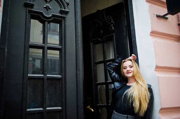 Blondes modisches Mädchen im langen schwarzen Ledermantel posierte gegen — Stockfoto