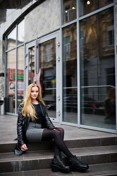 Blondes modisches Mädchen im langen schwarzen Ledermantel posierte am Stai — Stockfoto