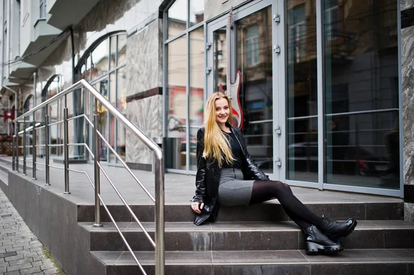 Blondes modisches Mädchen im langen schwarzen Ledermantel posierte am Stai — Stockfoto