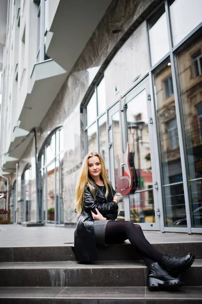 Blondes modisches Mädchen im langen schwarzen Ledermantel posierte am Stai — Stockfoto