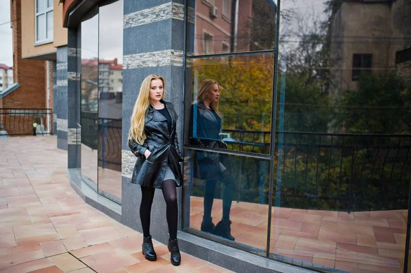Blond modieus meisje in lange zwarte leren jas gesteld tegen — Stockfoto