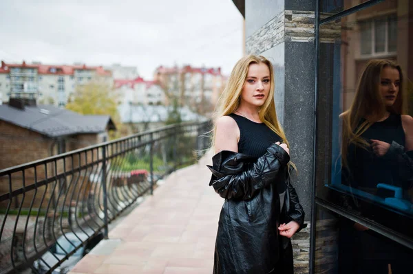 Blond fashionabla flicka i lång svart läder kappa poserade mot — Stockfoto