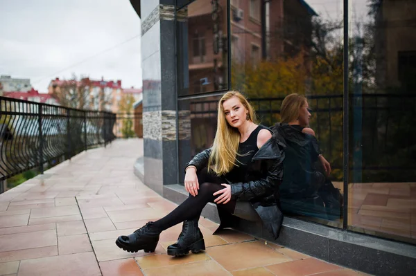 Blondes modisches Mädchen im langen schwarzen Ledermantel posierte gegen — Stockfoto