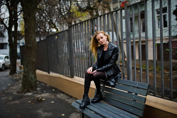 Blonde fashionable girl in long black leather coat posed on benc — Stock Photo, Image